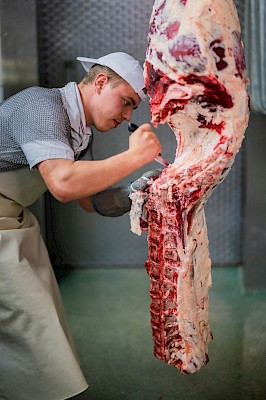 Metzger arbeitet an einem hängenden Fleischstück.