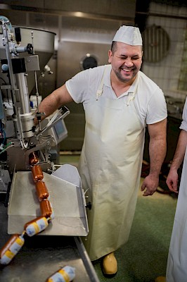 Metzger steht an einer Wurstmaschine und lacht.