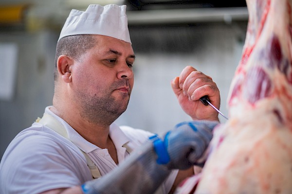 Ein Mitarbeiter in der Produktion arbeitet konzentriert an einem Fleischstück