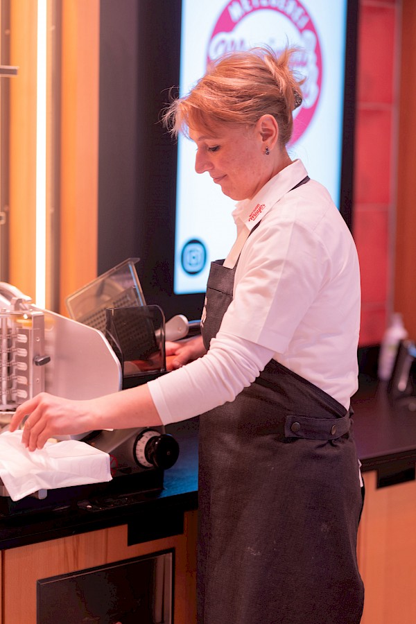 Eine Verkäuferin schneidet Wurst an einer Wurst-Schneide-Maschine.