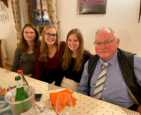 Friedrich Mayer mit seinen Enkellinnen am Tisch sitzend und in die Kamera lächelnd.