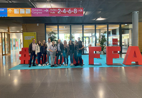 Familie Mayer steht vor einem Schild der Süddeutschen Fleischermesse und lächeln in die Kamera.
