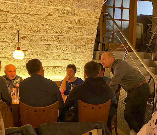 Frank Mayer steht an einem Tisch, an welchem Mitarbeiter der Metzgerei Mayer sitzen und sich untehalten.